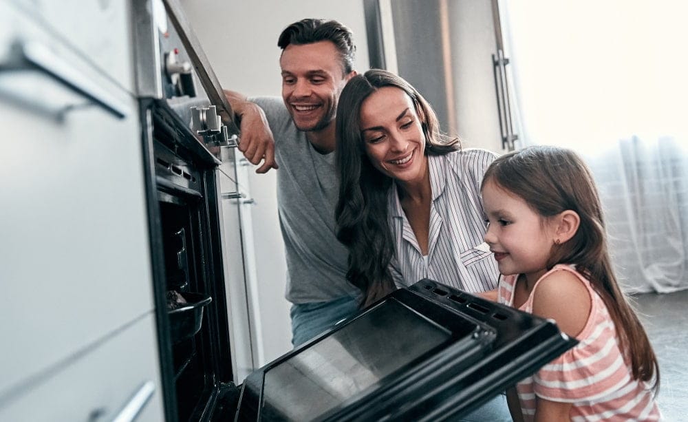 happy-young-family-with-their-little-cute-daughter-are-peep-into-oven-while-cooking-cakes-kitchen-min
